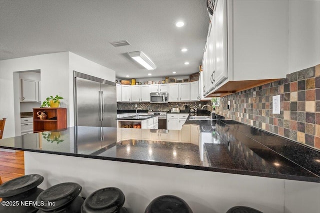 kitchen with white cabinetry, kitchen peninsula, a breakfast bar area, stainless steel appliances, and a textured ceiling