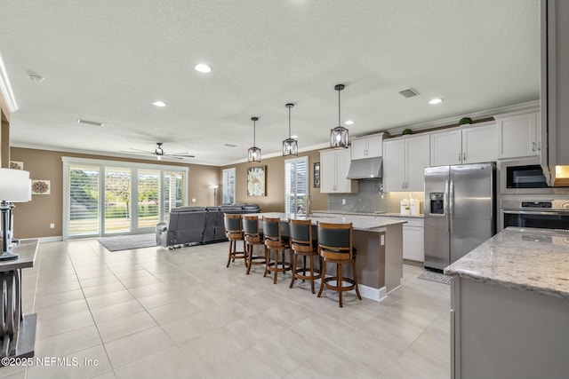 kitchen featuring ceiling fan, a kitchen island, pendant lighting, light stone countertops, and stainless steel appliances