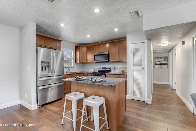 kitchen featuring a breakfast bar, dark stone counters, a center island, stainless steel appliances, and dark wood-type flooring