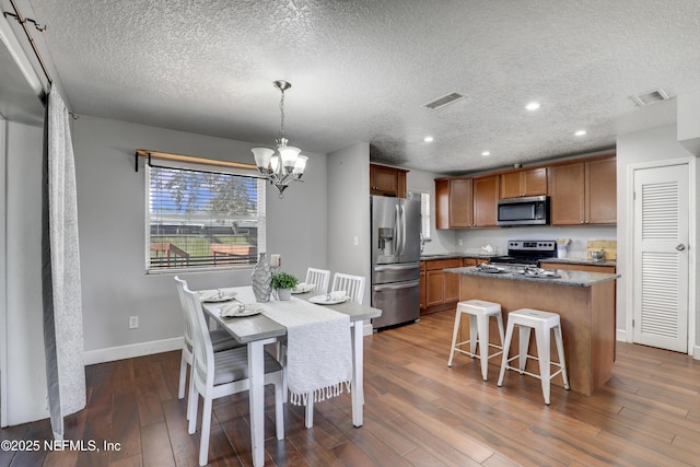 kitchen with pendant lighting, appliances with stainless steel finishes, an inviting chandelier, a center island, and dark hardwood / wood-style flooring