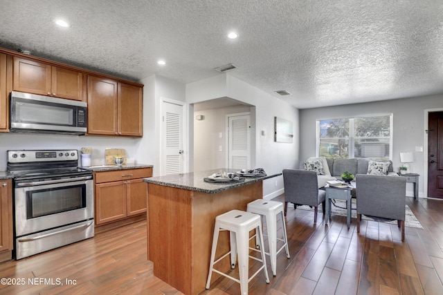 kitchen featuring a kitchen bar, a center island, a textured ceiling, dark hardwood / wood-style flooring, and stainless steel appliances