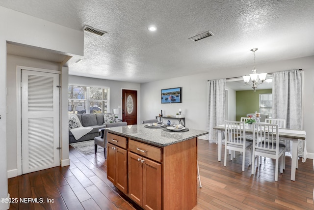 kitchen with an inviting chandelier, hanging light fixtures, dark hardwood / wood-style flooring, a kitchen island, and light stone countertops