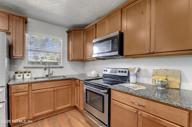 kitchen featuring sink, stainless steel appliances, light hardwood / wood-style floors, a textured ceiling, and dark stone counters