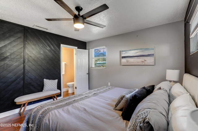 bedroom with wood-type flooring, ensuite bathroom, ceiling fan, and a textured ceiling