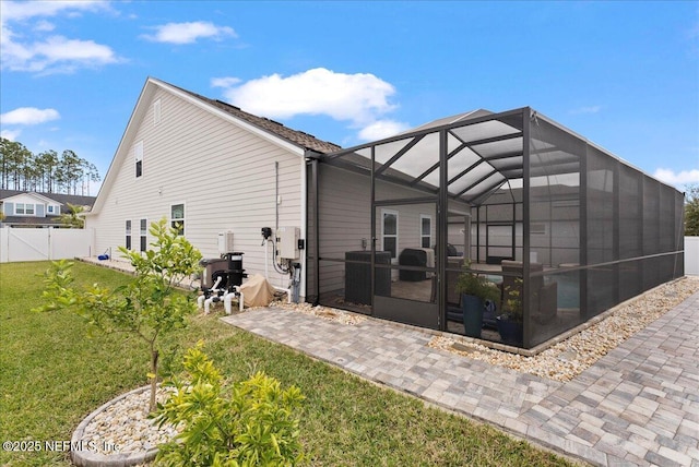 rear view of property featuring a yard, a patio area, and glass enclosure