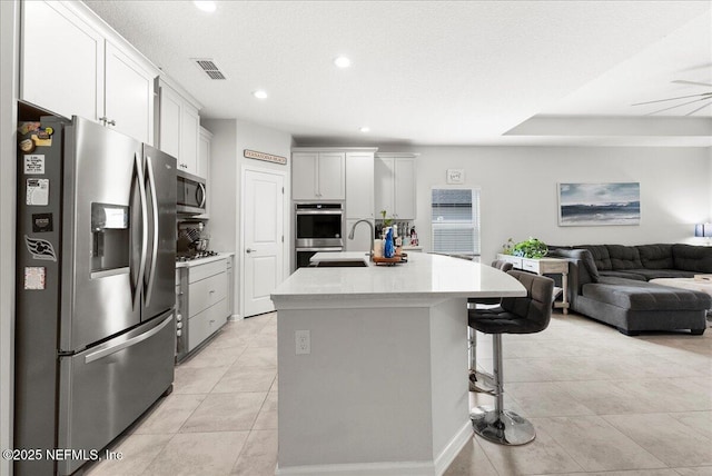 kitchen with sink, appliances with stainless steel finishes, a kitchen island with sink, a kitchen breakfast bar, and white cabinets