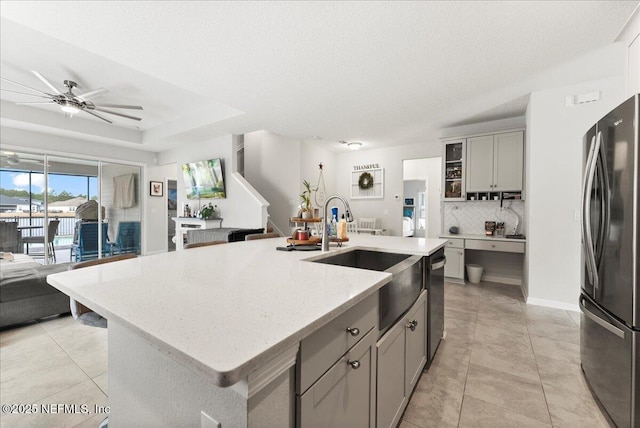 kitchen with sink, appliances with stainless steel finishes, gray cabinetry, backsplash, and an island with sink