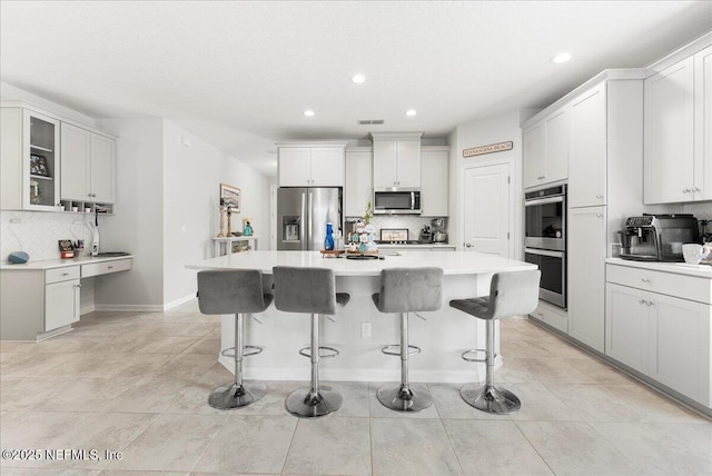 kitchen with a kitchen island, appliances with stainless steel finishes, white cabinets, and a kitchen bar