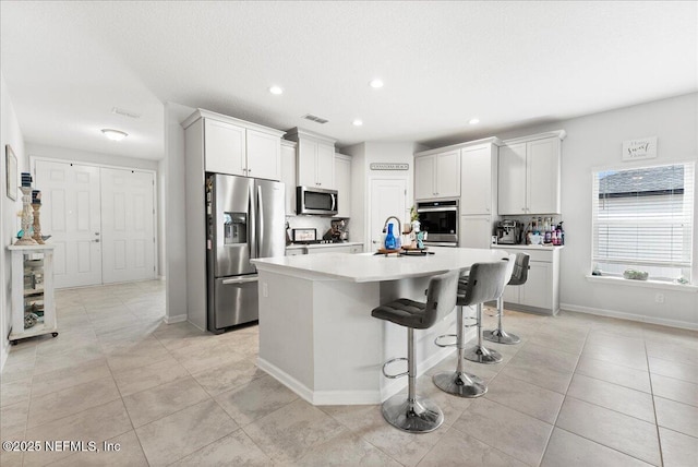 kitchen with appliances with stainless steel finishes, a kitchen island with sink, white cabinets, and a kitchen breakfast bar