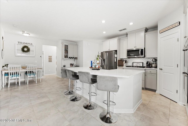 kitchen featuring a kitchen island with sink, a kitchen bar, backsplash, and appliances with stainless steel finishes