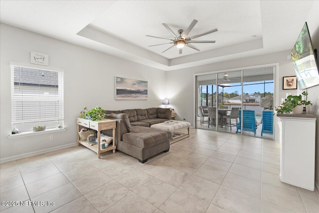 living room featuring ceiling fan, a raised ceiling, and light tile patterned floors