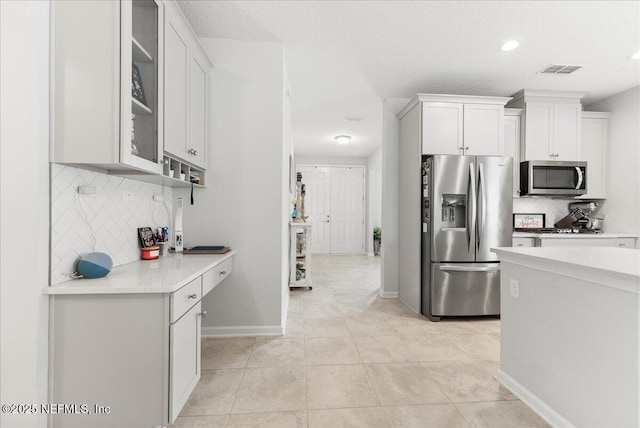 kitchen featuring tasteful backsplash, white cabinetry, appliances with stainless steel finishes, and light tile patterned floors