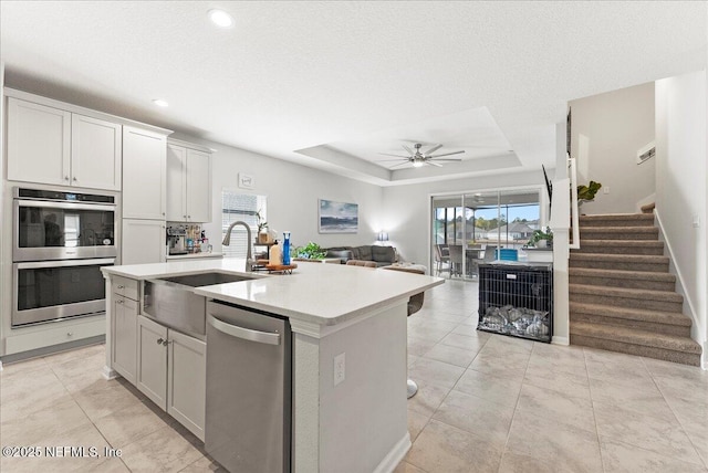 kitchen with sink, white cabinetry, a raised ceiling, stainless steel appliances, and a kitchen island with sink