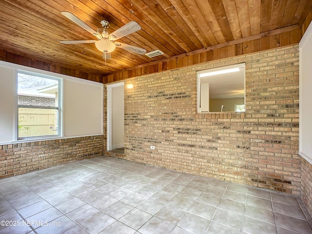 tiled empty room featuring ceiling fan, brick wall, and wood ceiling