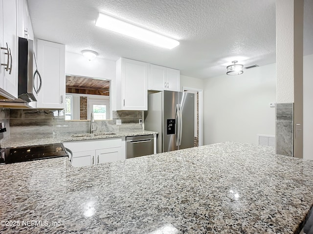 kitchen featuring white cabinetry, kitchen peninsula, stainless steel appliances, a textured ceiling, and sink