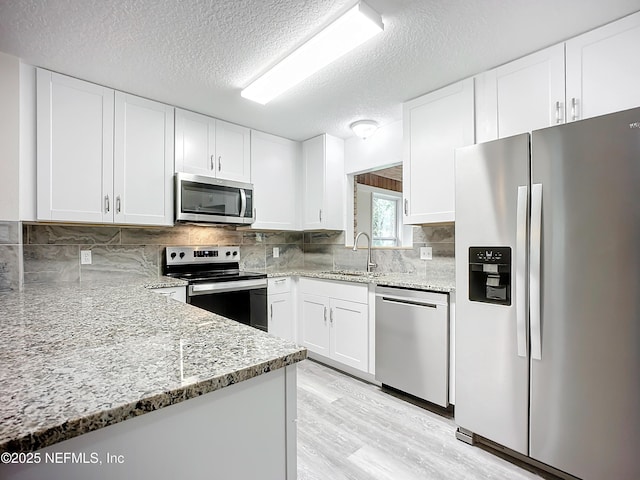 kitchen featuring stainless steel appliances, light stone countertops, a textured ceiling, white cabinets, and sink