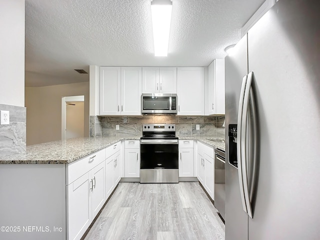 kitchen featuring white cabinets, appliances with stainless steel finishes, decorative backsplash, kitchen peninsula, and light stone counters