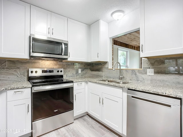 kitchen with light stone countertops, a textured ceiling, white cabinetry, stainless steel appliances, and sink