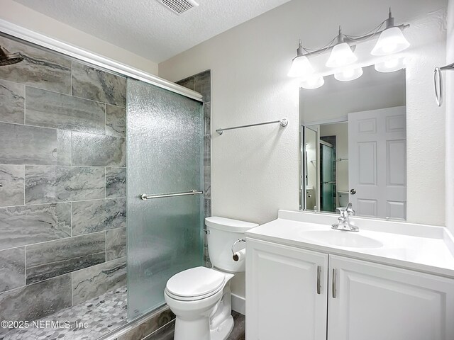 bathroom with toilet, vanity, a shower with door, and a textured ceiling