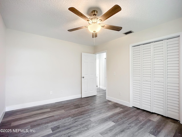 unfurnished bedroom with ceiling fan, a textured ceiling, dark hardwood / wood-style flooring, and a closet