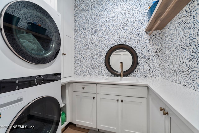 clothes washing area featuring cabinets, sink, and stacked washer and dryer