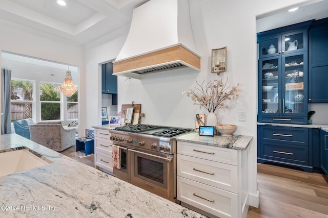 kitchen with blue cabinetry, double oven range, white cabinets, and custom range hood