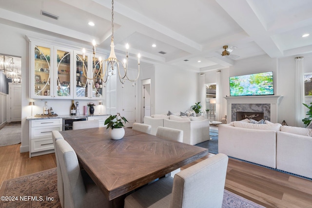 dining area featuring light hardwood / wood-style floors, coffered ceiling, ceiling fan, a fireplace, and beamed ceiling