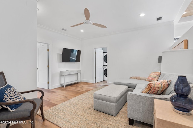 living room with ceiling fan, wood-type flooring, stacked washer and clothes dryer, and ornamental molding