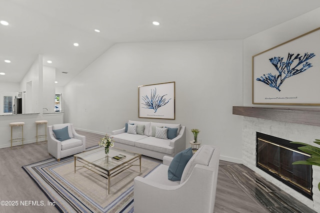 living room featuring hardwood / wood-style flooring, a stone fireplace, and lofted ceiling