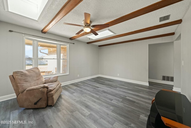 living area featuring beam ceiling, ceiling fan, dark hardwood / wood-style flooring, and a textured ceiling