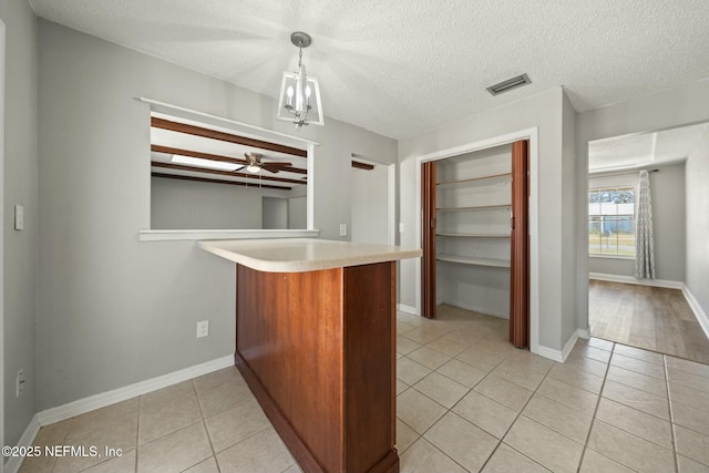 kitchen with ceiling fan with notable chandelier, pendant lighting, kitchen peninsula, and light tile patterned flooring