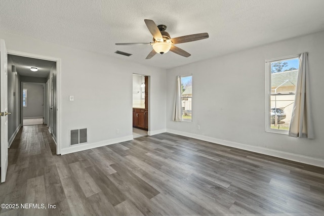 empty room with ceiling fan, plenty of natural light, a textured ceiling, and dark hardwood / wood-style flooring