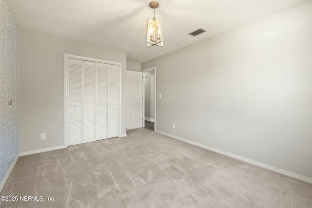 unfurnished bedroom with light carpet, a closet, a notable chandelier, and a textured ceiling