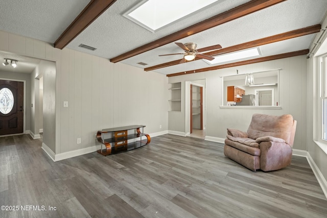 living area featuring hardwood / wood-style flooring, a textured ceiling, beam ceiling, and ceiling fan