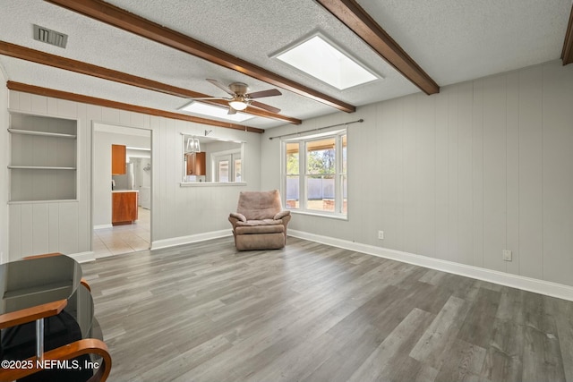 sitting room with light hardwood / wood-style floors, a textured ceiling, beam ceiling, and ceiling fan