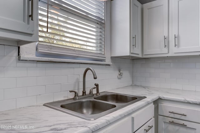 kitchen featuring light stone counters, sink, backsplash, and white cabinets