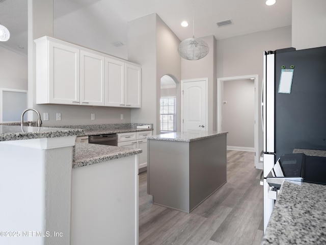 kitchen with a kitchen island, white cabinetry, hanging light fixtures, stainless steel refrigerator, and light stone counters