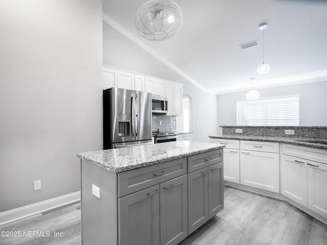 kitchen with white cabinets, appliances with stainless steel finishes, a center island, decorative light fixtures, and backsplash