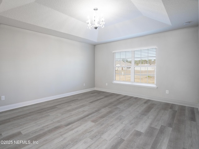 spare room with a notable chandelier, a tray ceiling, and a textured ceiling