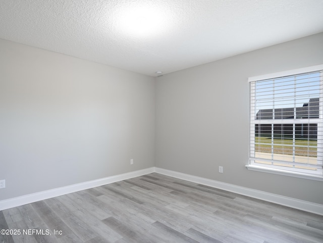 empty room featuring a textured ceiling, a wealth of natural light, and light hardwood / wood-style floors