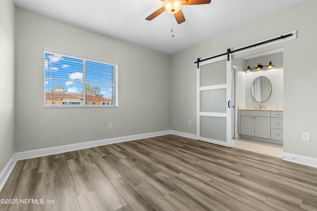 unfurnished bedroom featuring ceiling fan, a barn door, light hardwood / wood-style flooring, and ensuite bath