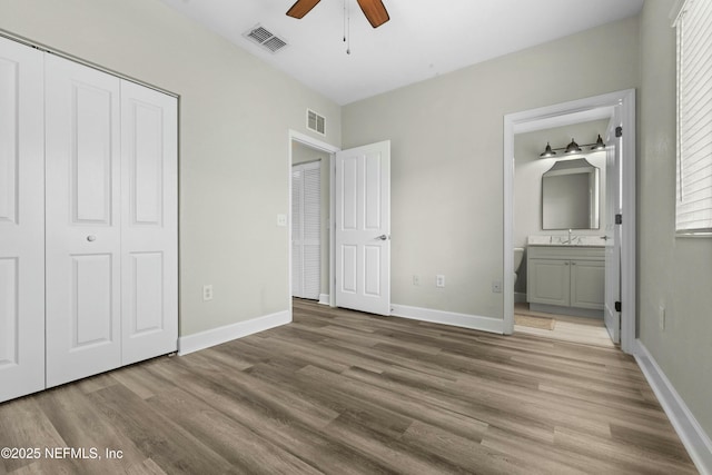 unfurnished bedroom featuring ceiling fan, wood-type flooring, ensuite bathroom, and a closet