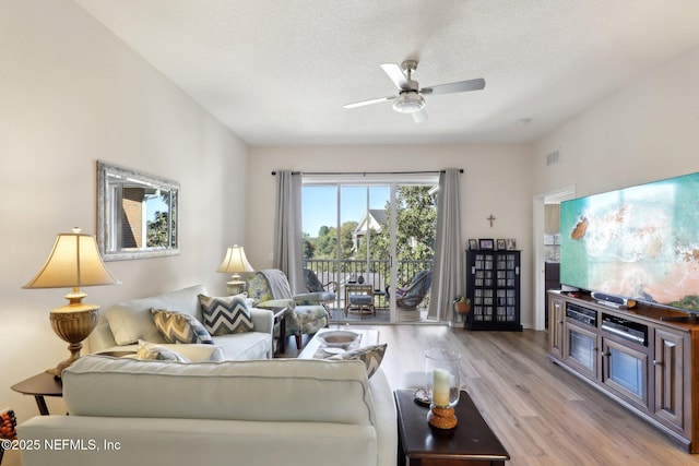 living room with ceiling fan, a textured ceiling, and light wood-type flooring