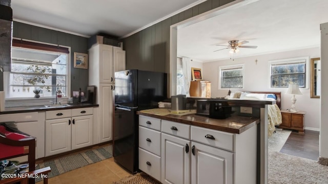 kitchen featuring freestanding refrigerator, ceiling fan, a sink, white cabinetry, and crown molding