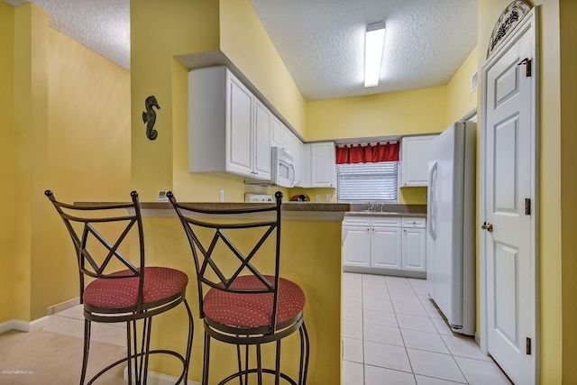 kitchen with white appliances, a textured ceiling, white cabinetry, sink, and light tile patterned flooring