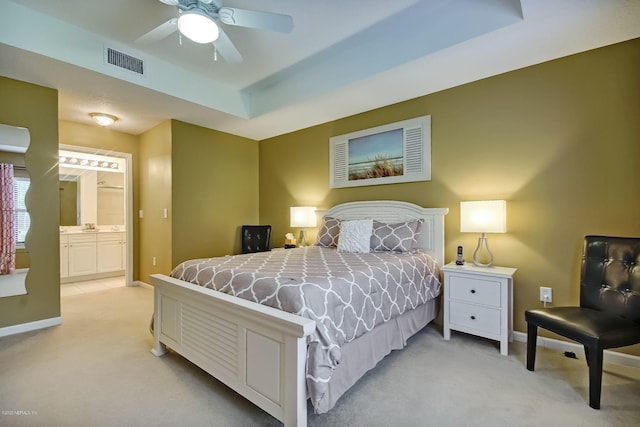 bedroom with ensuite bathroom, ceiling fan, light carpet, and a tray ceiling