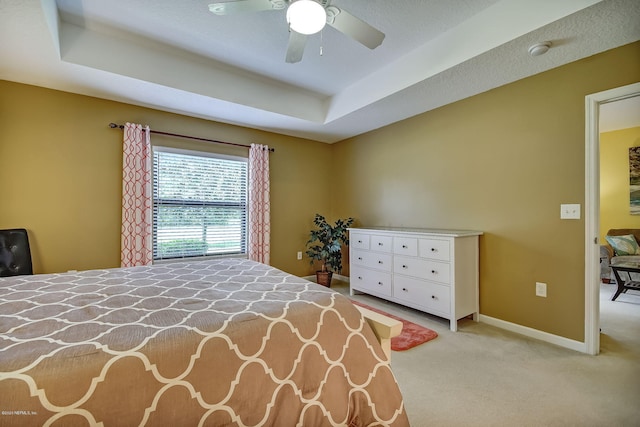 bedroom with ceiling fan, light carpet, and a tray ceiling