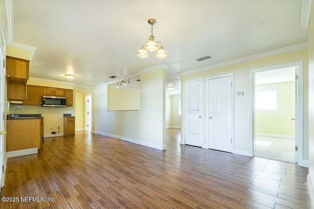 unfurnished living room featuring ornamental molding, sink, dark hardwood / wood-style flooring, and a notable chandelier