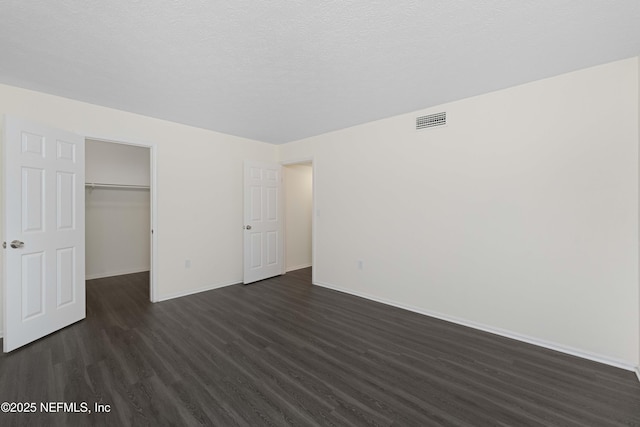 unfurnished bedroom with a textured ceiling, dark hardwood / wood-style floors, a closet, and a walk in closet