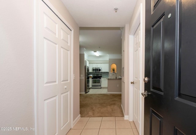 corridor featuring light tile patterned flooring, light colored carpet, baseboards, and a sink